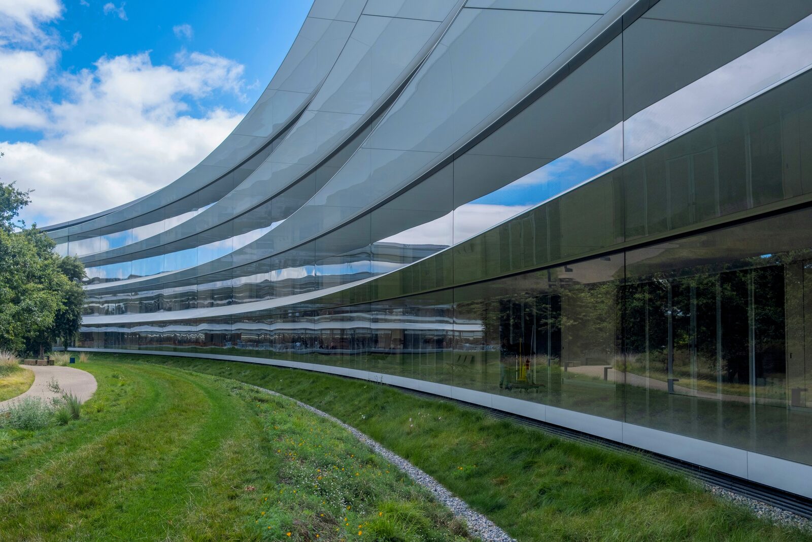 Geschwungene Glasfassade des Apple Park, in der sich Himmel und Wolken spiegeln